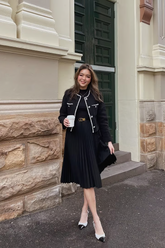 a lady wears a black crop jacket with a midi black pleated skirt